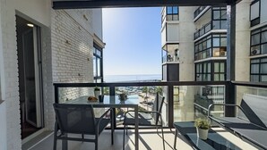 Un balcon avec une table et des chaises en verre, un pot de fleurs et une vue sur la mer et les bâtiments.