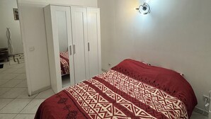 A bedroom with a bed, a wardrobe, a wall-mounted light, and a door leading to another room. - Close to Paris and Disney, Self-contained apartment (Le Perreux-sur-Marne)