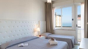 A hotel room with a large bed, a smaller bed, a nightstand with a lamp, and a view of the sea through a large window. - Hotel La Perla (Rimini)