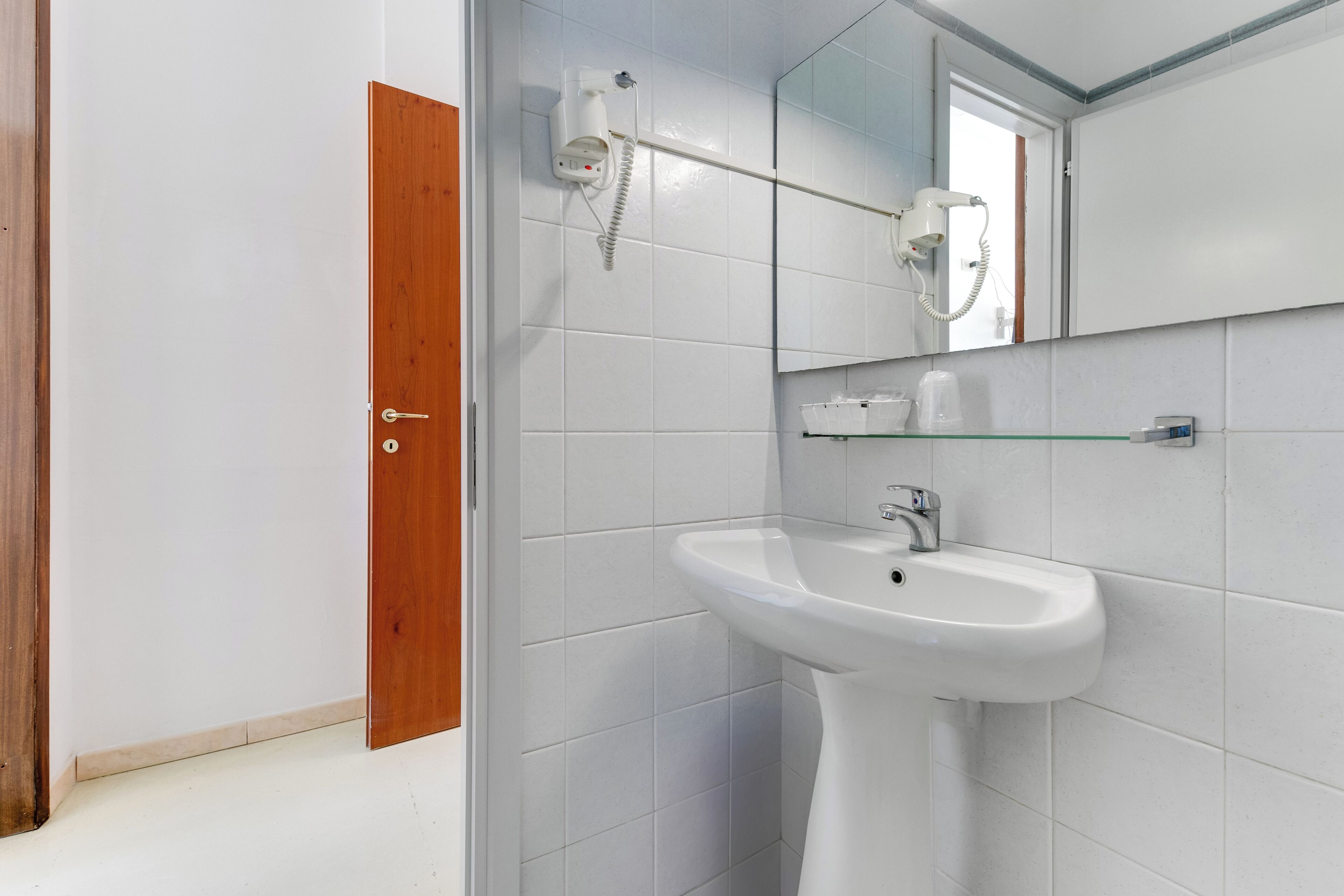 Un baño con un lavamanos blanco, un espejo y un perchero para toallas.