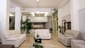 A spacious living room with a white sofa set, a glass coffee table, and a kitchen area in the background. - Hotel La Perla (Rimini)