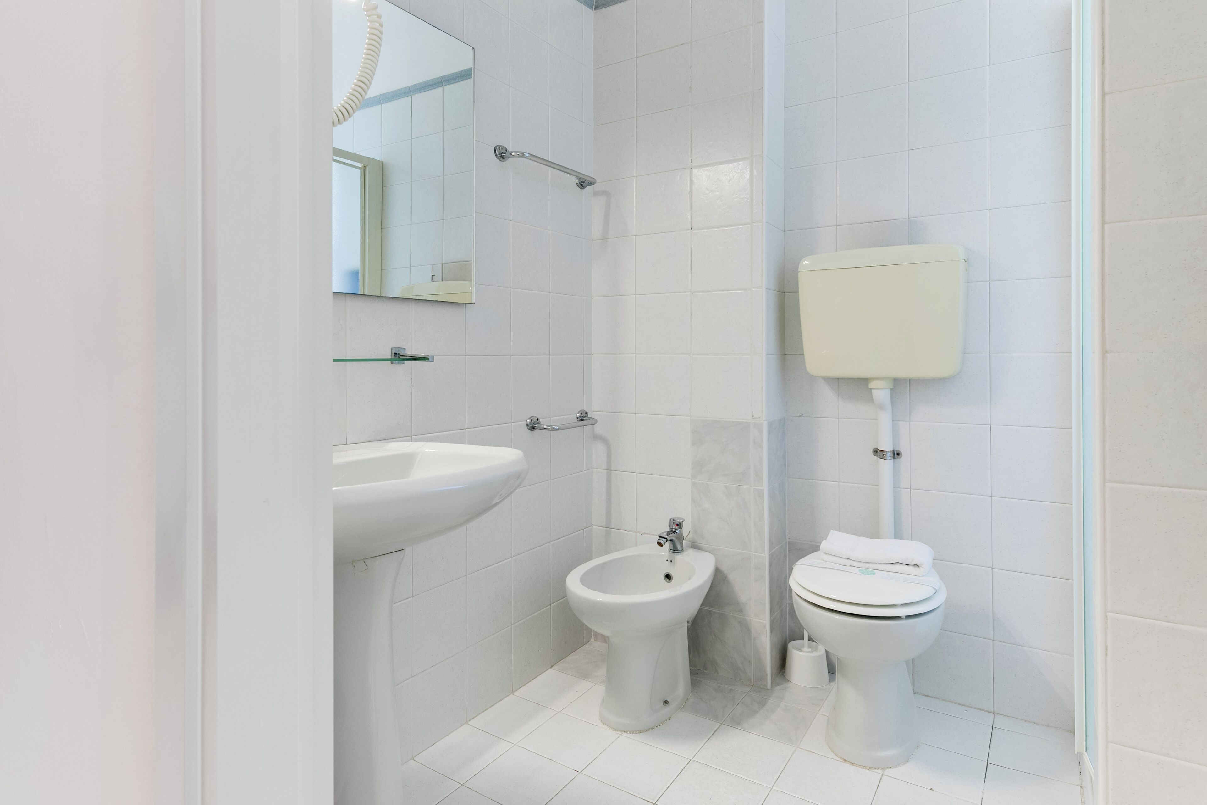 Un baño moderno con lavamanos, bidé e inodoro blancos, todo con accesorios cromados.