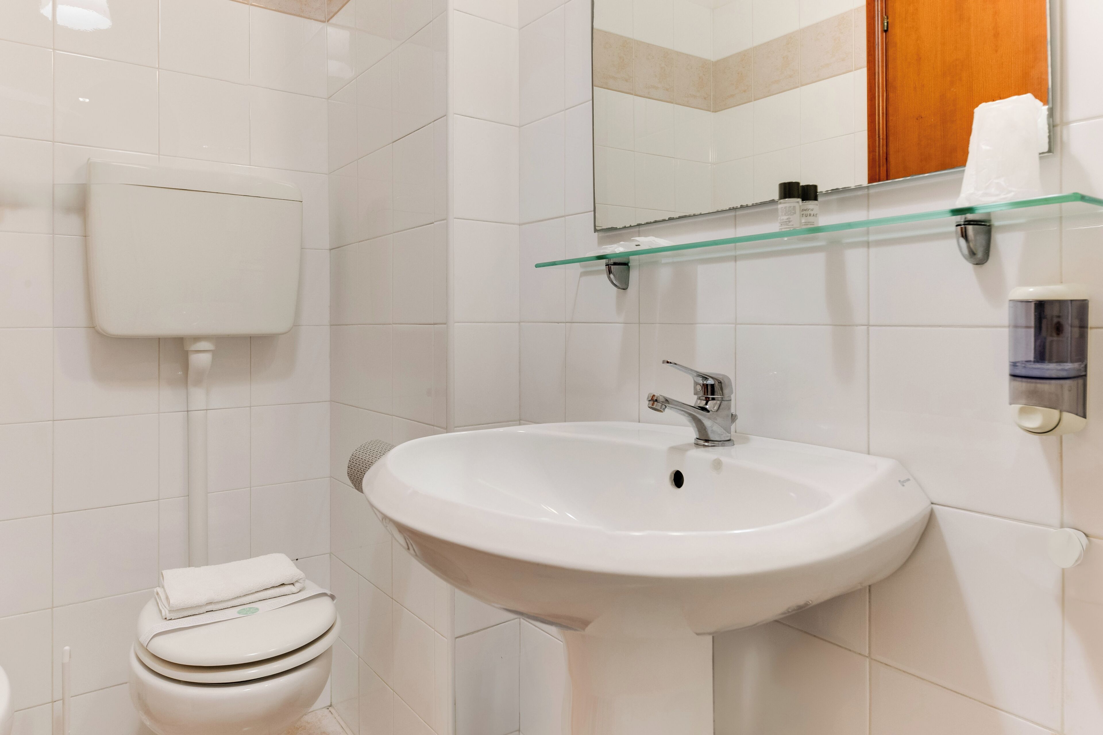 A bathroom with a white toilet, a white sink, and a glass shelf above the sink.