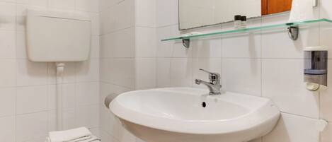 A bathroom with a white toilet, a white sink, and a glass shelf above the sink.