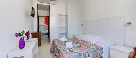 A bedroom with a bed, a desk, a chair, a wardrobe, and an air conditioning unit.