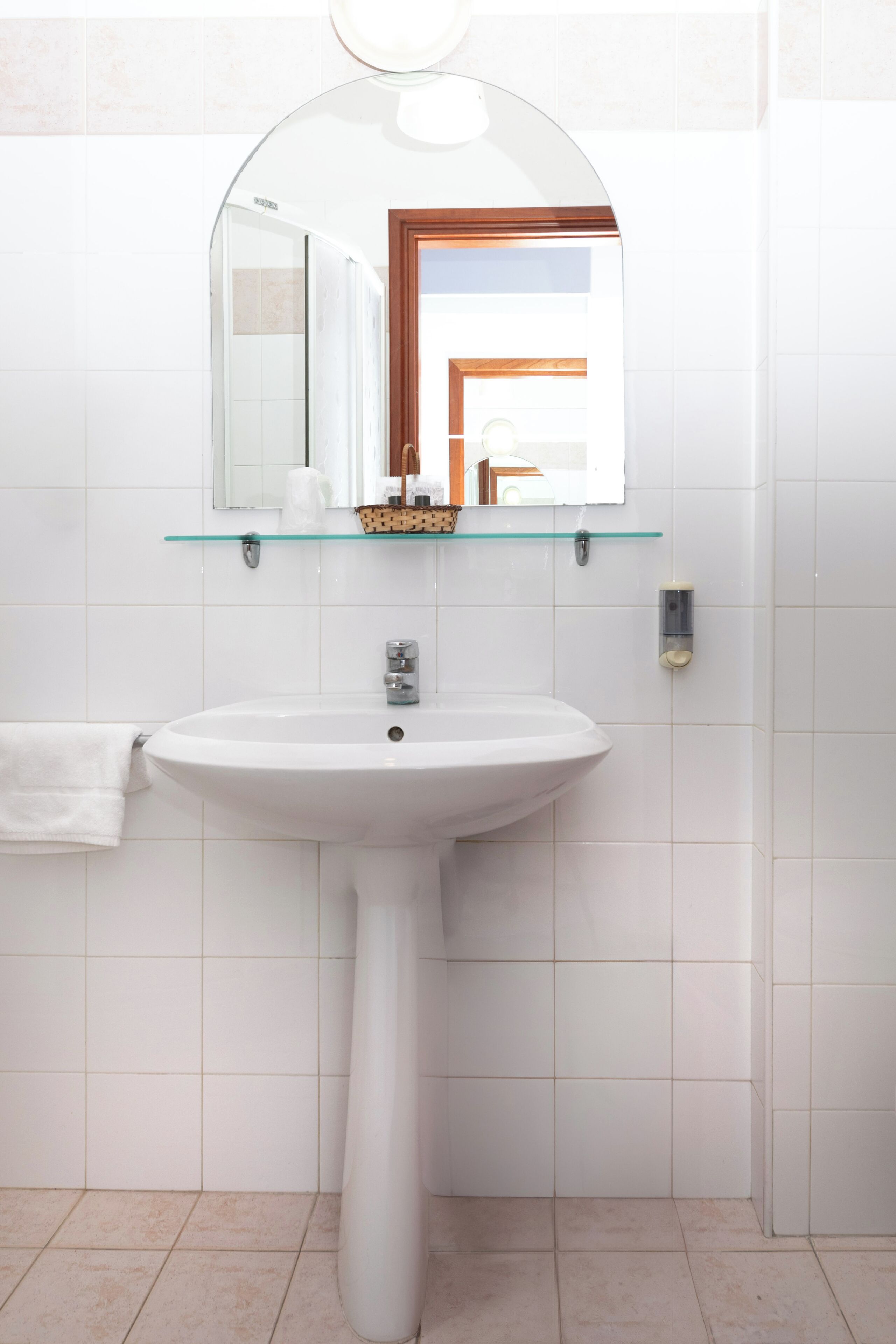 Une salle de bain avec un lavabo sur pied blanc, une étagère en verre au-dessus du lavabo et un miroir avec un cadre en bois.