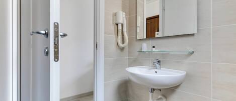 A modern bathroom with a white sink, a glass shelf, and a hairdryer mounted on the wall.