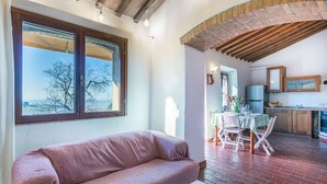 A cozy living room with a sofa, a dining area with a table and chairs, a kitchen with cabinets and a refrigerator, and a large window with a view of trees. - Wonderful private villa for 6 people with hot tub, WIFI, terrace, pets allowed and panoramic view (Castellina Marittima)