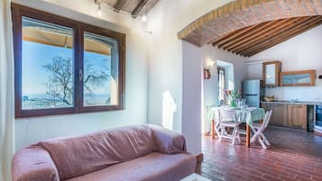 Un accogliente soggiorno con divano, una zona pranzo con tavolo e sedie, una cucina con pensili e frigorifero, e un'ampia finestra con vista sugli alberi.