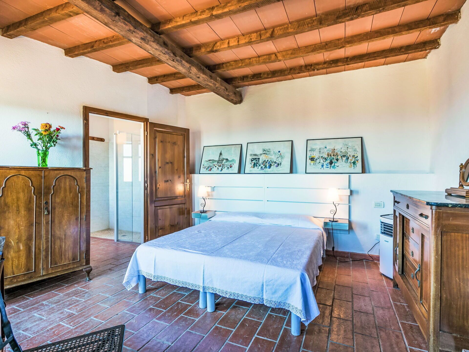 A bedroom with a bed, wooden wardrobe, and a desk with a lamp.