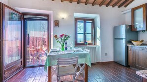 A dining area with a table set for two, a kitchen with a refrigerator, and a view through a window. - Wonderful private villa for 6 people with hot tub, WIFI, terrace, pets allowed and panoramic view (Castellina Marittima)