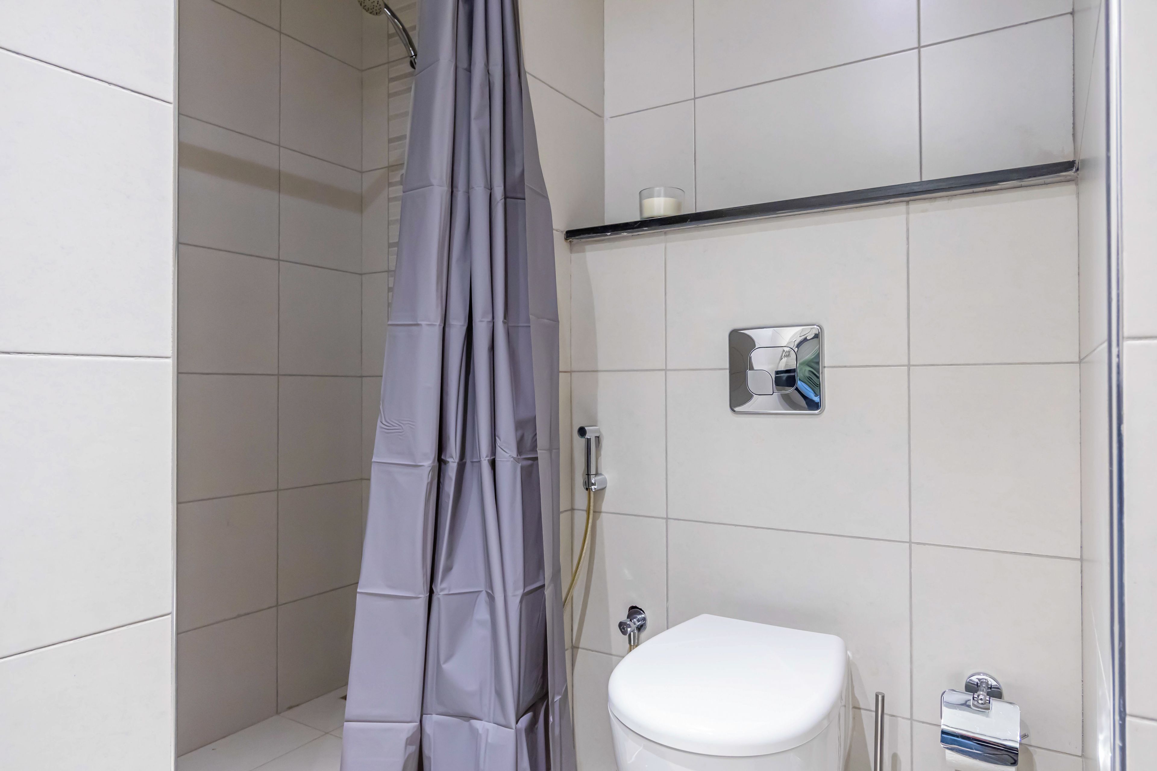 A bathroom with a shower curtain, a toilet, and a shelf with toiletries.