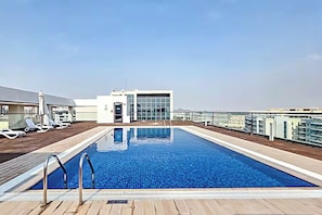 Una piscina sul tetto con vista chiara sullo skyline della città, sedie a sdraio e un edificio con pareti di vetro.