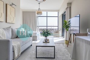 A modern living room with a sofa, coffee table, and a large window offering a view of the city. - Bloomfields Cozy STU The View Raha (Abu Dhabi)