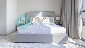 Een moderne slaapkamer met een groot bed, een nachtkastje en uitzicht op de stad door het raam.