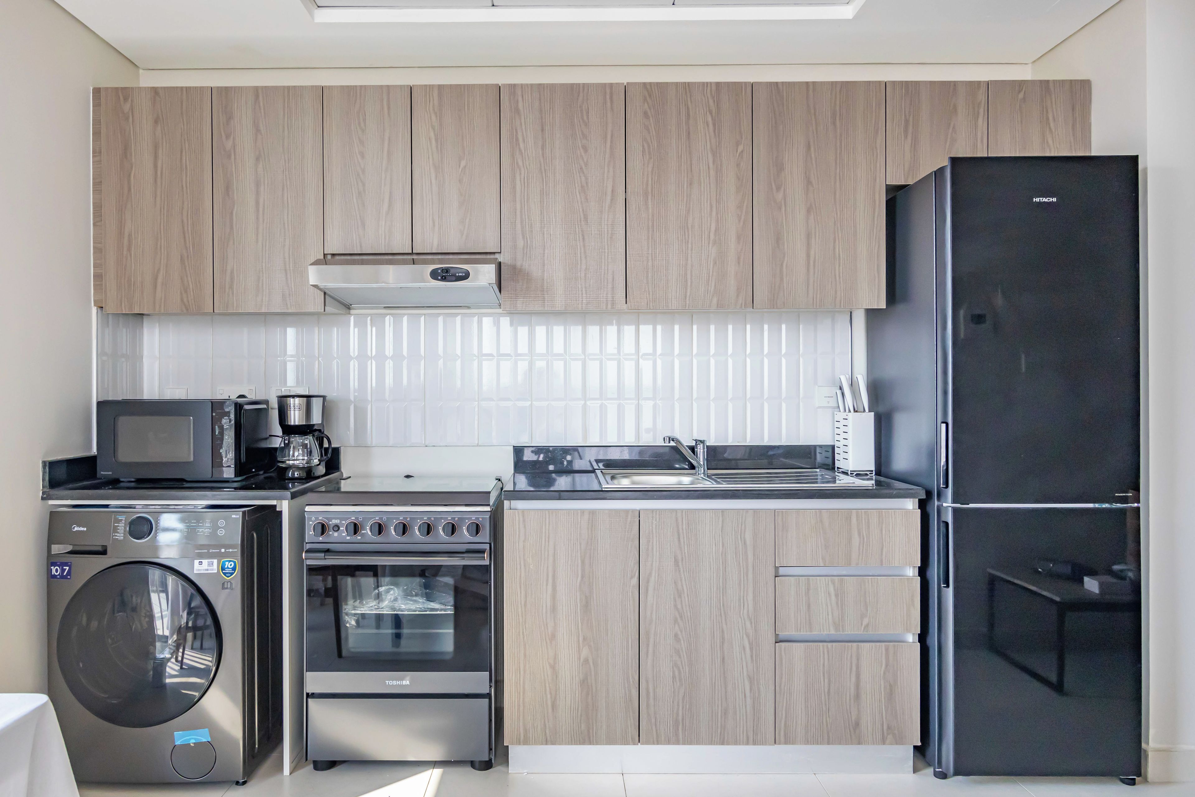 A modern kitchen with wooden cabinets, a built-in microwave, a coffee maker, a stove, an oven, and a refrigerator.