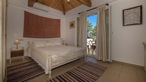 Une chambre avec un plafond en bois, un lit recouvert d’une couvre-lit à motifs, une table de chevet avec une lampe, un tapis à motifs et une vue sur l’extérieur par une porte.