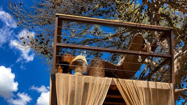 Une pergola en bois, agrémentée d’un hamac, de tissus drapés et de guirlandes lumineuses suspendues.