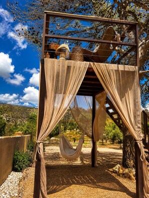 A wooden pergola with a hammock, draped fabric, and hanging lights.