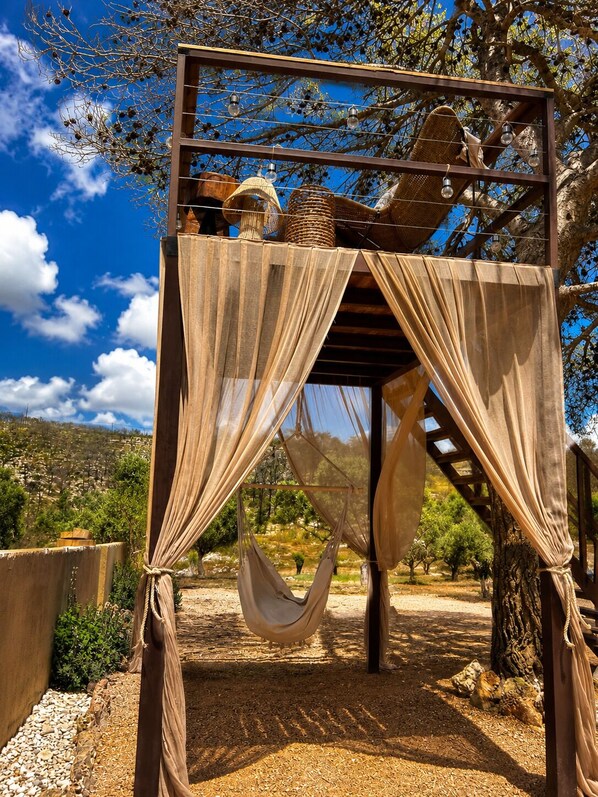 Una pérgola de madera con una hamaca, tela colgante e iluminación.