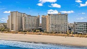 Un hotel frente a la playa con varios edificios altos, una playa de arena y olas del océano.