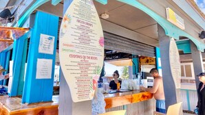 Un bar junto a la playa con un cartel que muestra bebidas y cócteles.