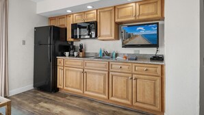 Una cocina con armarios de madera, un refrigerador negro, un microondas y un televisor de pantalla plana montado sobre la encimera.