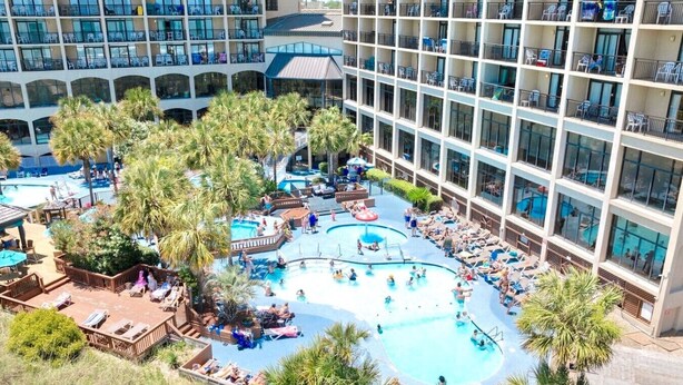 A hotel with multiple swimming pools, sun loungers, and palm trees. - Oceanfront Condo with Resort Pools (North Myrtle Beach)