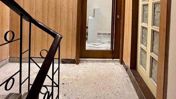 Un couloir intérieur en bois, avec un escalier menant à une porte portant l’inscription « Sarai Inn ».