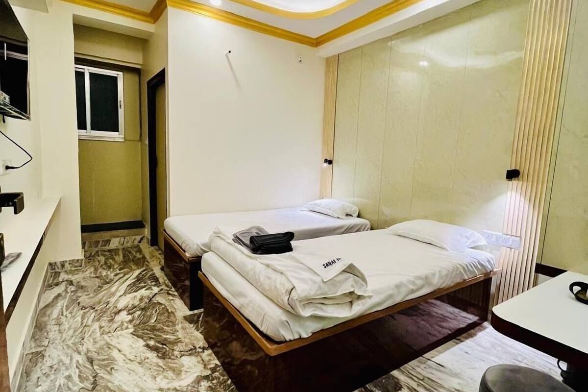 Quarto de hotel com piso de mármore, duas camas, um ventilador de teto e uma pequena mesa com uma cadeira.