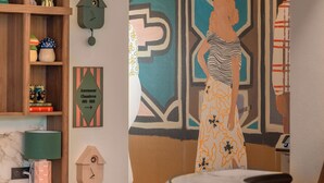 A room with a wooden bookshelf, a wall clock, a decorative wall piece, and a painting of a woman. - Chachacha Hôtel (Nantes)