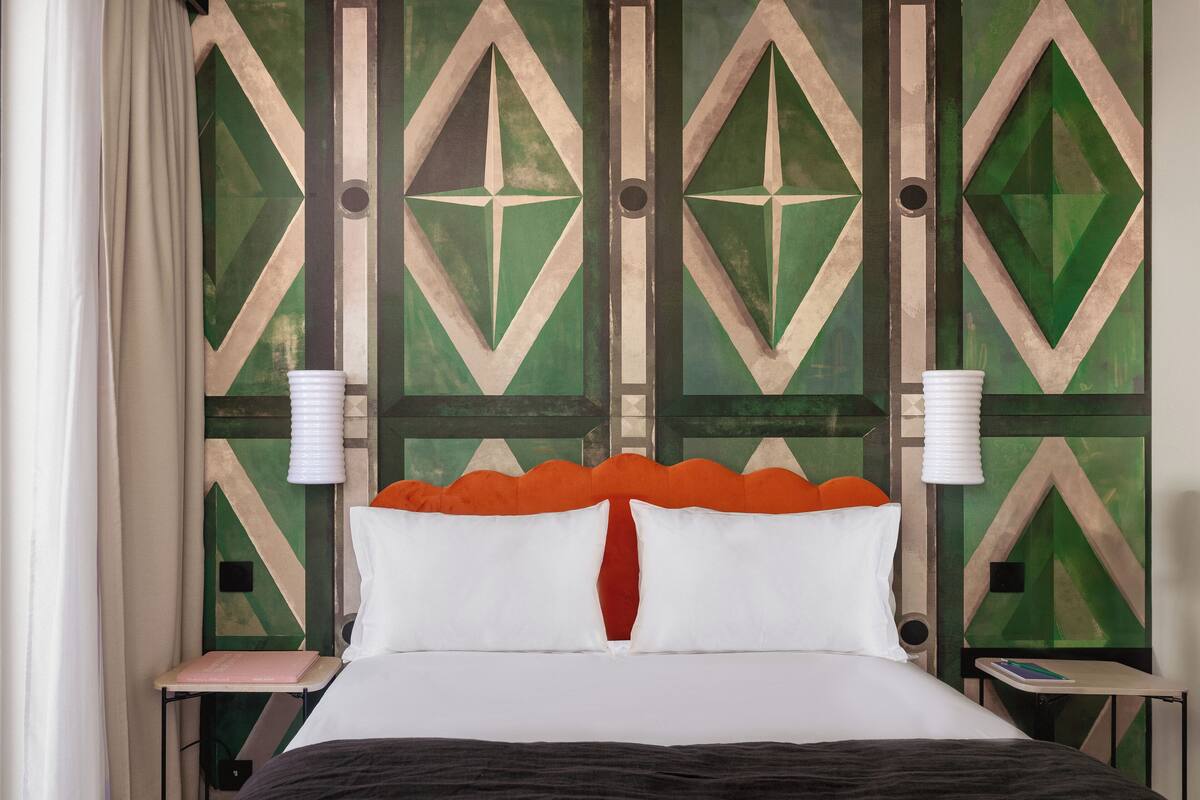 A bed with white and red pillows, a black headboard, and a green and beige geometric wall design.