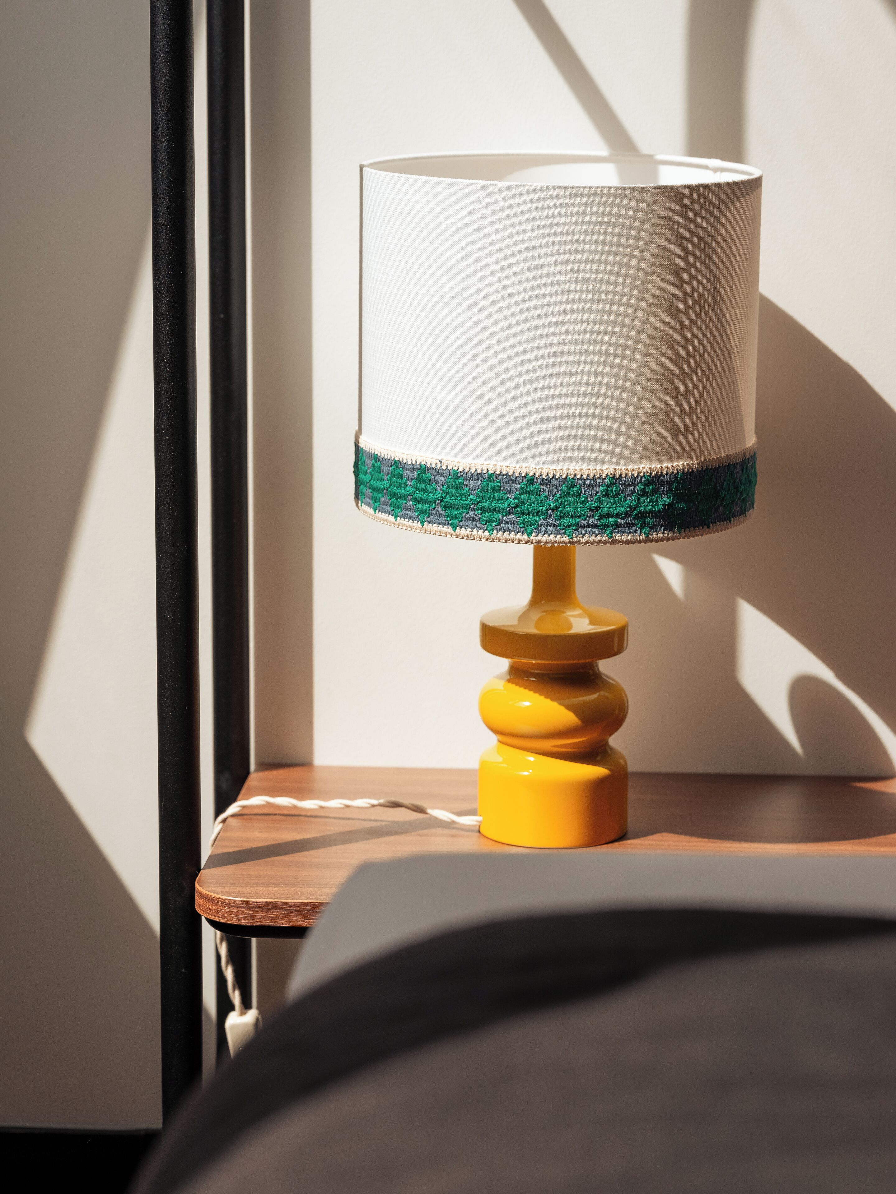 A lamp with a white shade and a green trim on a wooden nightstand.