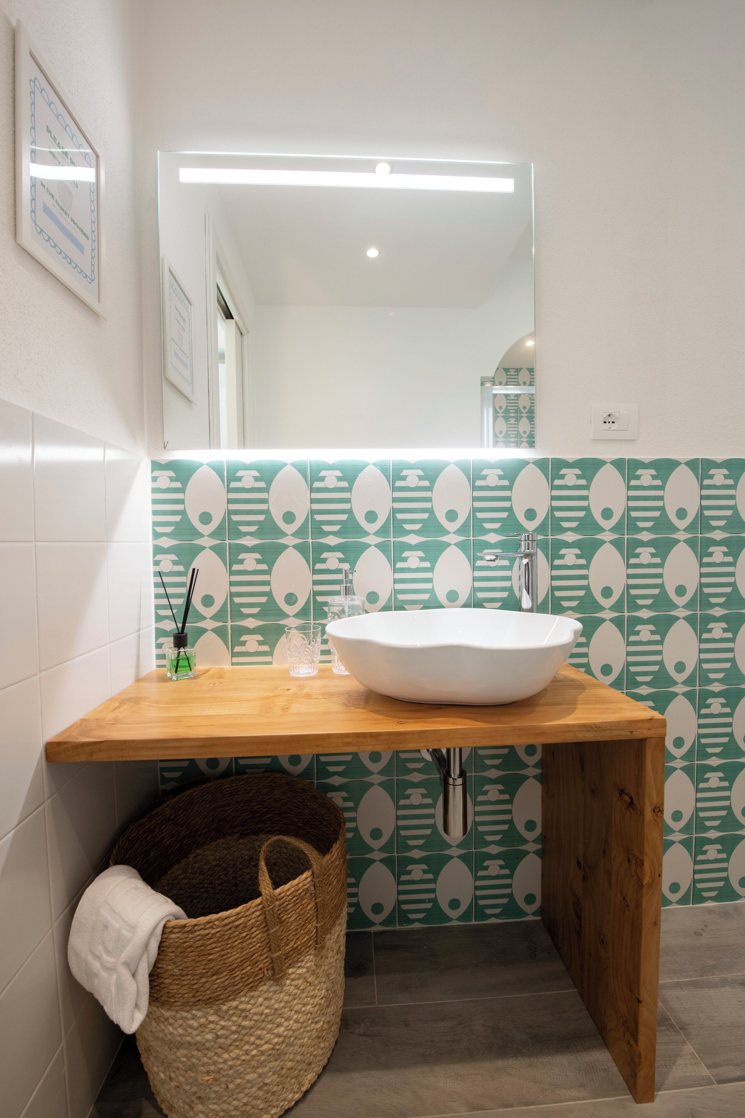Une salle de bain avec un meuble-lavabo en bois, un lavabo blanc et un pare-feu vert à motifs.