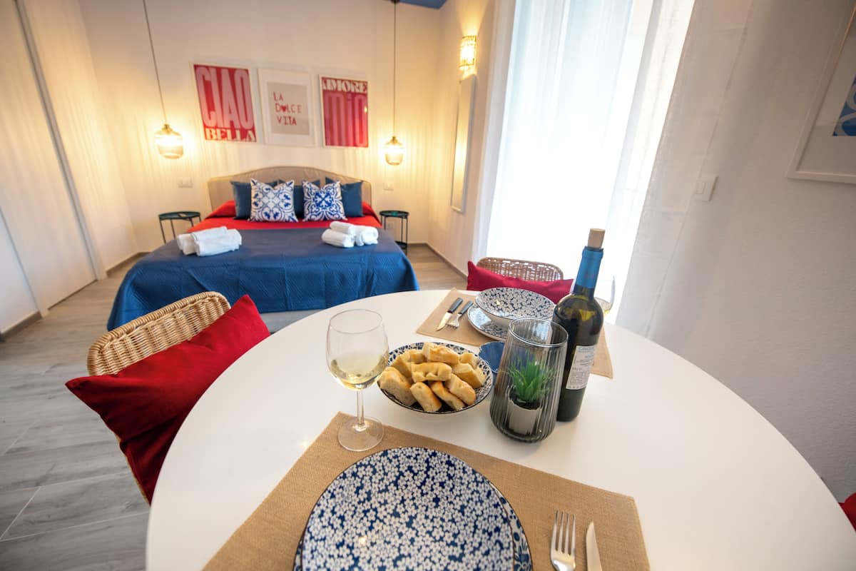 Une chambre à coucher bien rangée, avec un lit, une table de chevet et un coin repas où une table est dressée pour deux personnes.