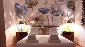 A neatly made bed with folded towels, two bedside tables with lamps, and a floral mural on the wall. - Charming 2-bedroom apartment in lovely Firenze with AC, WiFi (Florence)