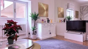 A living room with a glass coffee table, a potted plant, a white cabinet, a flat-screen TV, and decorative items on a shelf. - Charming 2-bedroom apartment in lovely Firenze with AC, WiFi (Florence)