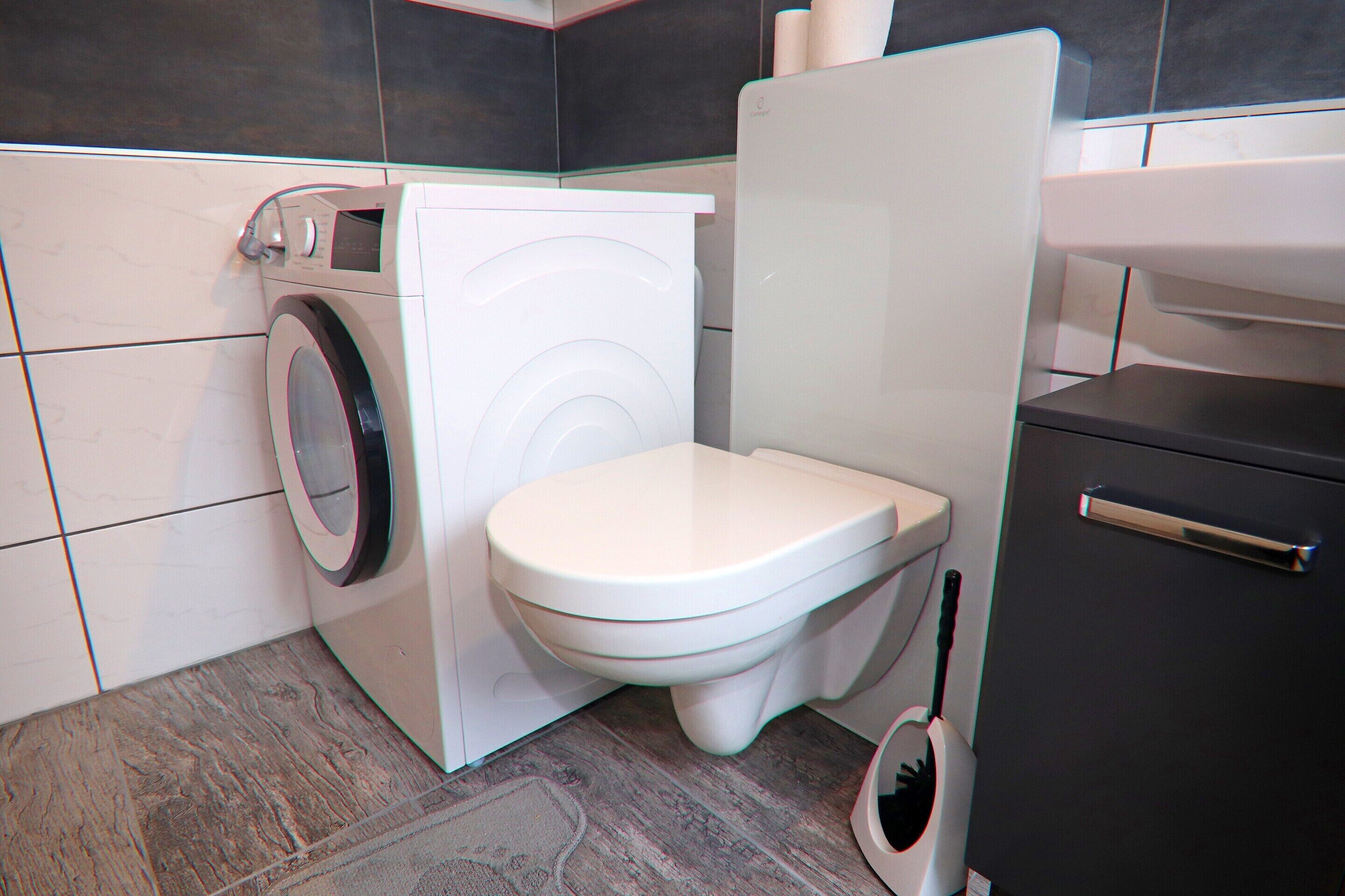 A compact bathroom with a washing machine, toilet, and a cabinet.