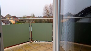 A balcony with a glass door, a metal railing, and a view of houses in the background. - Ferienwohnung Kranichring in Negast Nahe Stralsund (Steinhagen)