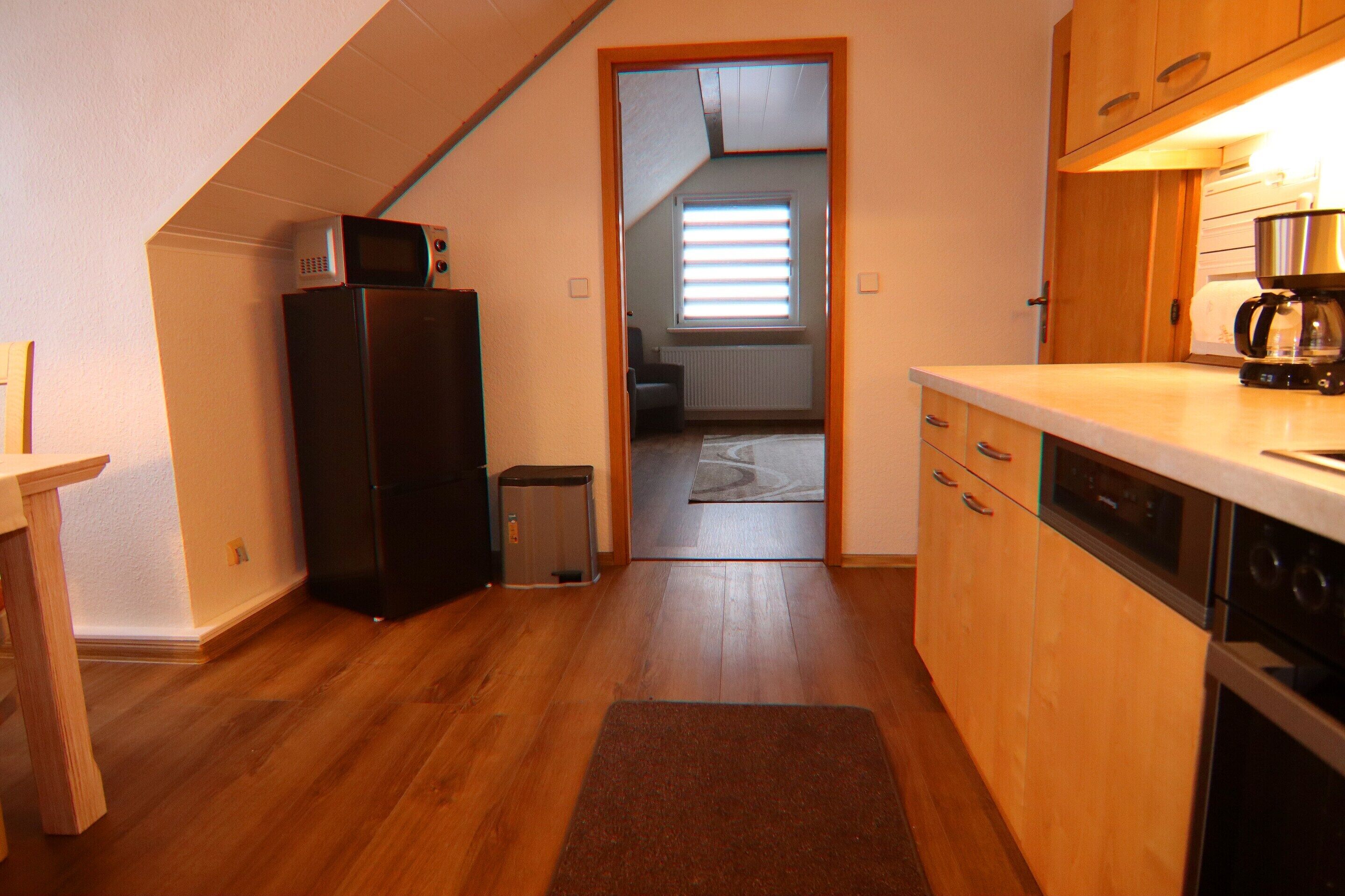 Una cocina compacta con armarios de madera, microondas integrado, cafetera y un cubo de basura.