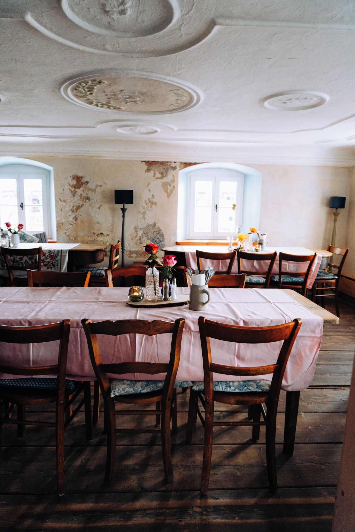 A dining area with wooden chairs and tables, a chandelier, and a vintage ceiling.