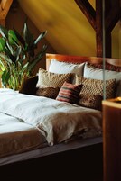 Uma cama bem arrumada com várias almofadas e uma planta grande ao lado.