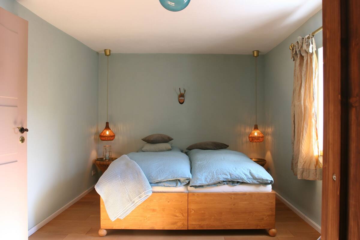 A bedroom with a wooden bed, two bedside lamps, a wall-mounted animal head decoration, and a door on the left.
