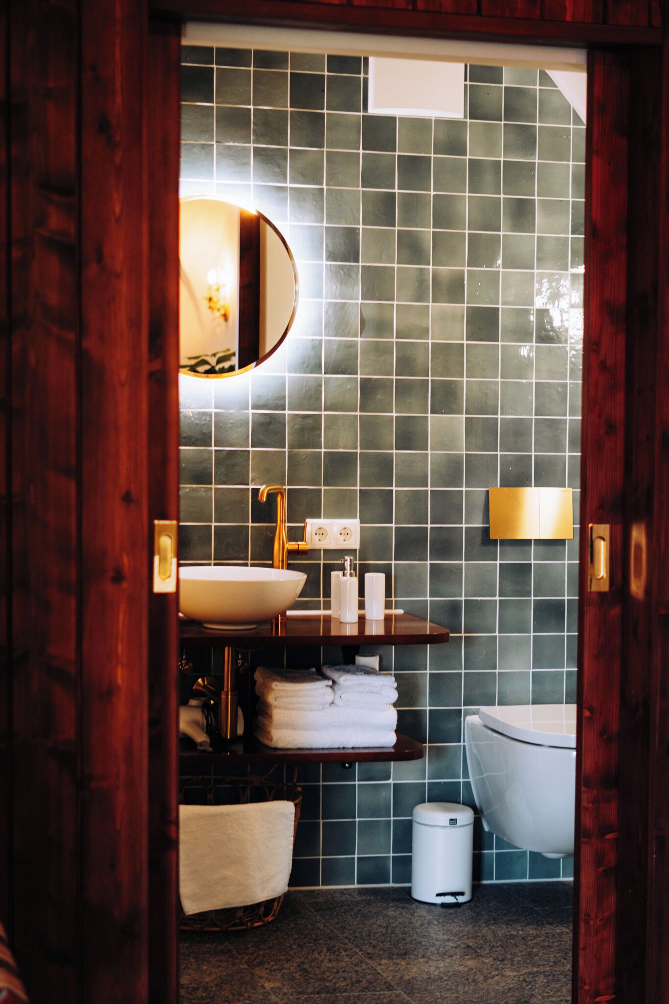 A bathroom with a wooden door, a white sink, a mirror, a towel rack, and a toilet.