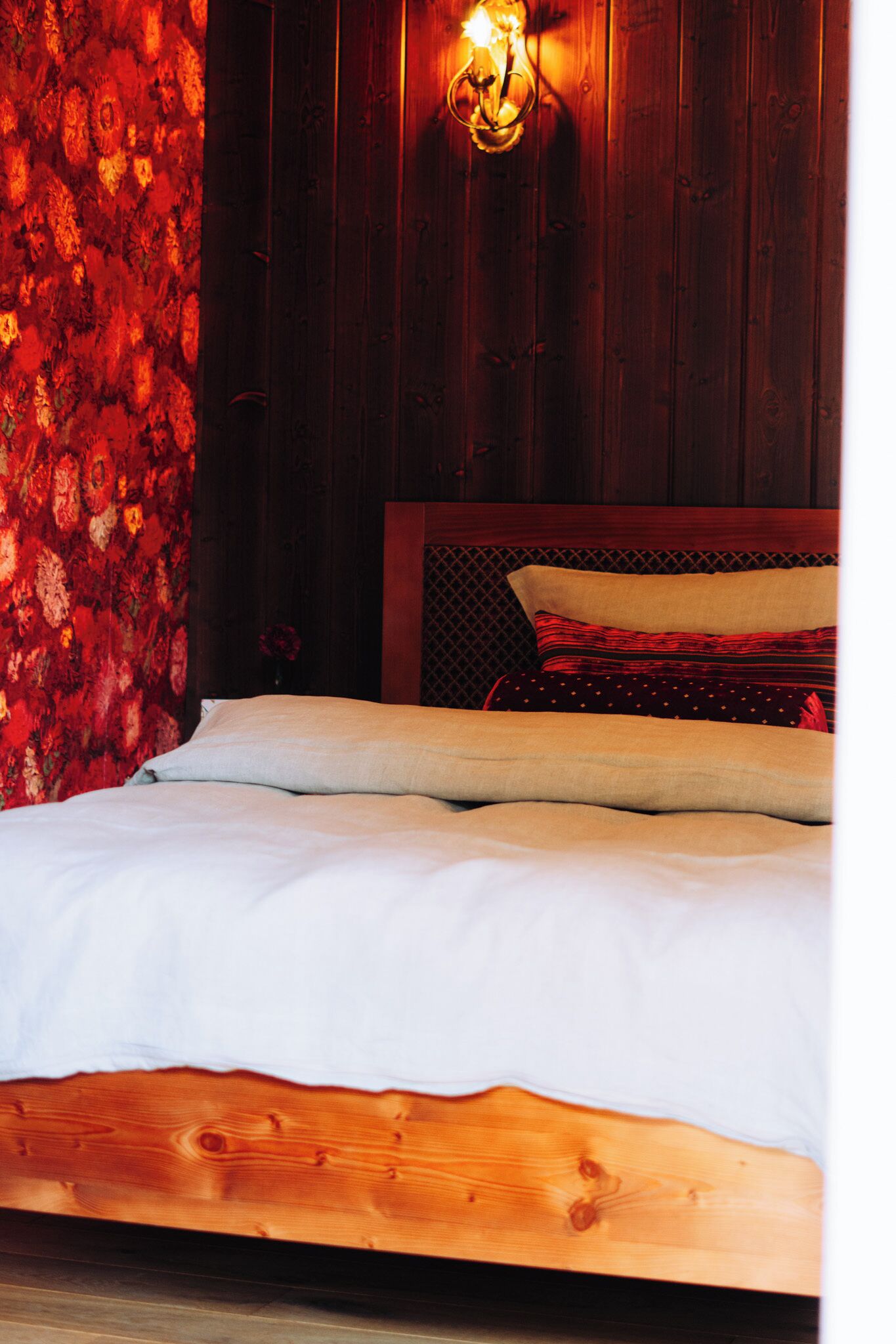 A bed with a wooden frame and white bedding in a room with wooden walls and a red textured wall on one side.