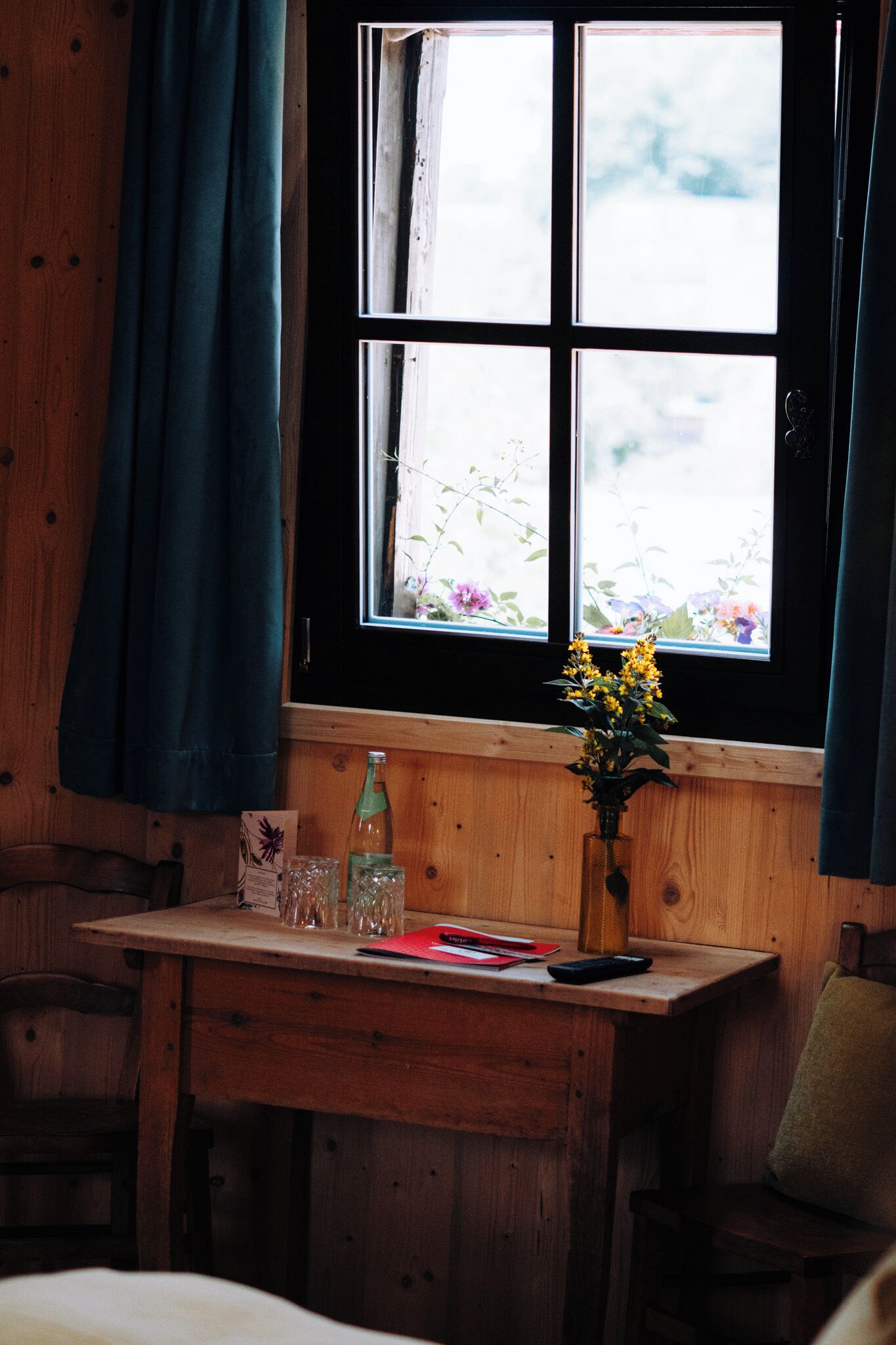 Une pièce en bois avec une fenêtre, un bureau, une chaise et un vase rempli de fleurs.