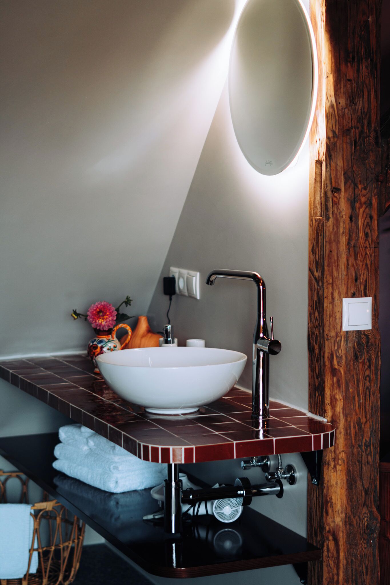 A modern bathroom with a white sink, a wooden vanity, and a mirror with a light.