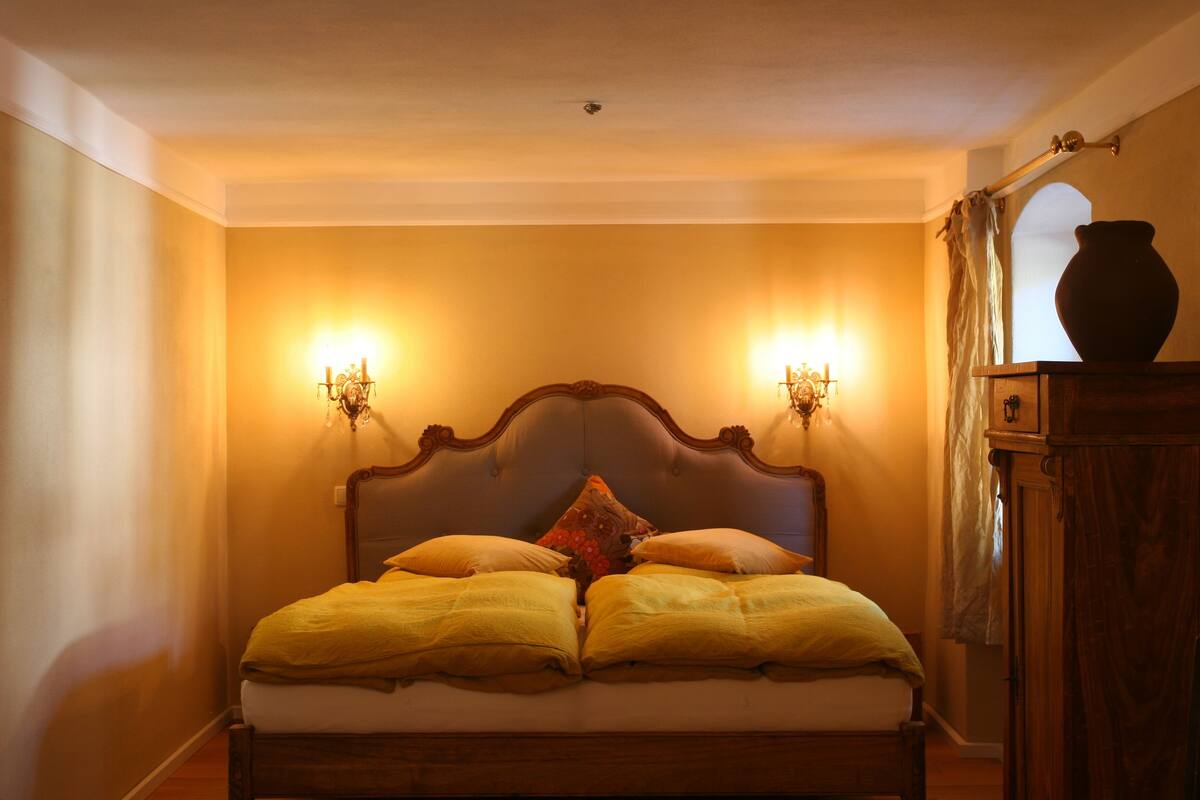 A bedroom with a wooden bed, two wall-mounted lamps, and a vase on a cabinet.
