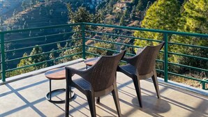 Una terrazza con due poltrone in vimini e un tavolino, affacciata su un paesaggio montuoso con edifici e alberi.