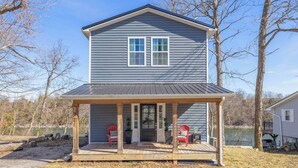 A two-story house with a covered porch, a front door, and two red Adirondack chairs.